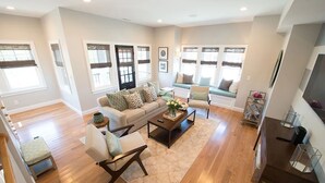 A spacious living room with a sofa, armchairs, a coffee table, and a TV.