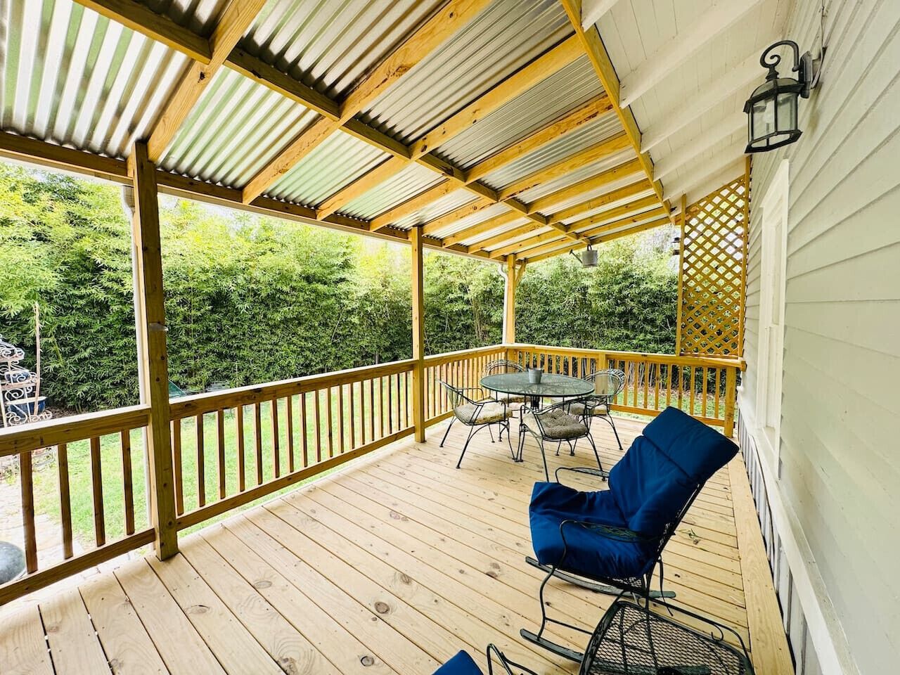 Una terraza techada al aire libre con suelo de madera, una mesa con sillas y una silla azul.