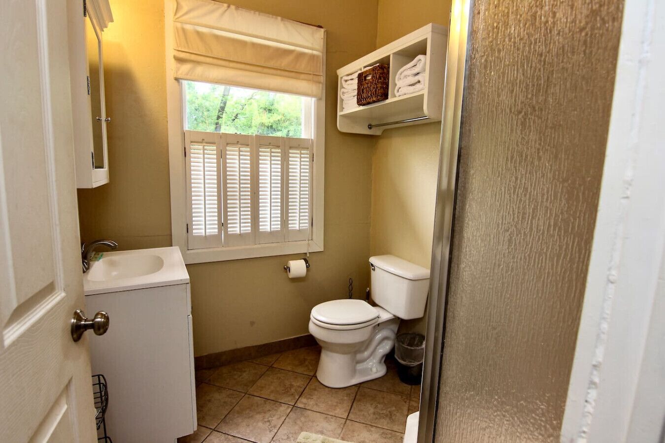Een kleine badkamer met toilet, wastafel en raam met luiken.