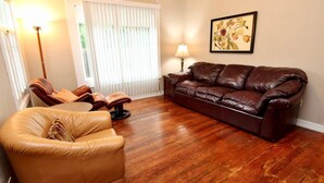 Una sala de estar con un sofá de cuero marrón, un sillón de cuero color beige y una lámpara de pie.