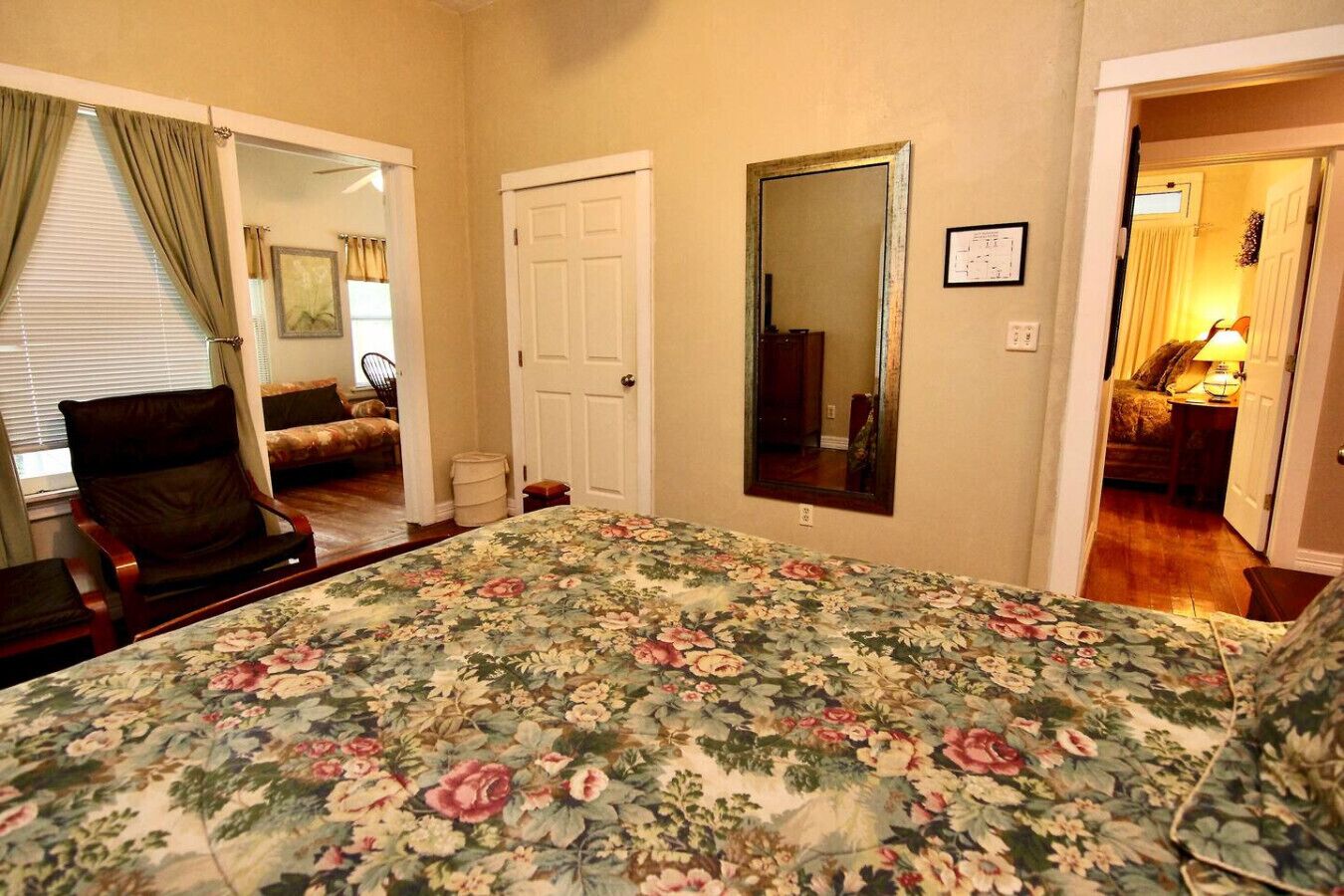 A bedroom with a floral bedspread, a chair, a door, and a mirror.