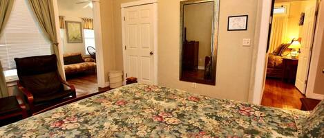 A bedroom with a floral bedspread, a chair, a door, and a mirror.
