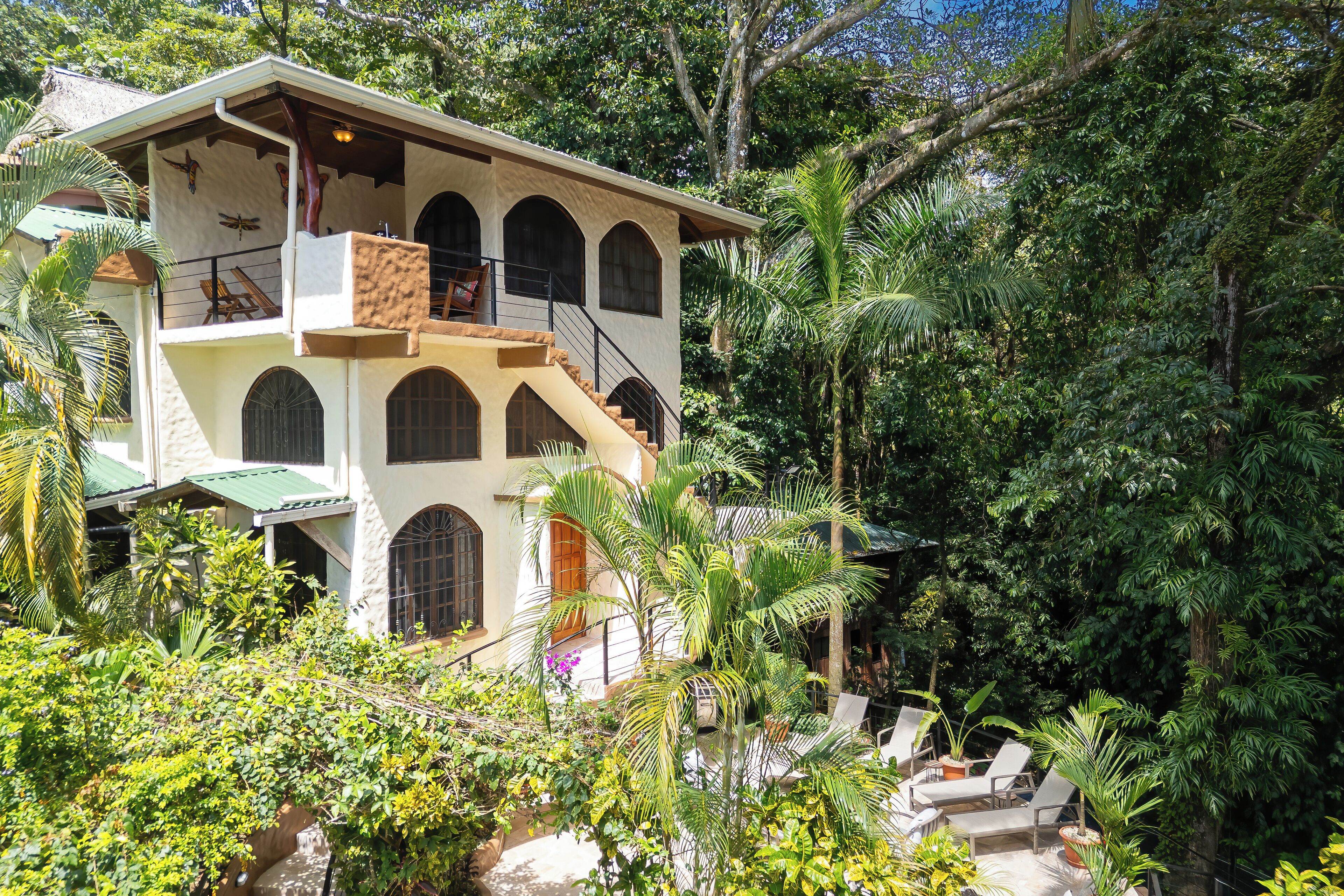 A two-story building with a balcony, surrounded by lush greenery and palm trees.