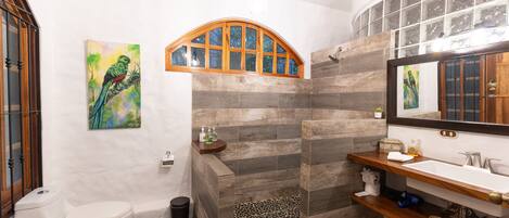 A bathroom with a white toilet, a shower with a wooden arch, a sink with a mirror, and a tiled floor.