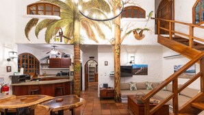 Ein geräumiger Wohnbereich mit einer Holztreppe, einer Küche mit Bar und einem Essbereich mit Holztischen.