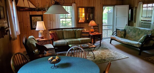 A cozy cabin interior with a wooden interior, a round table with a bowl of fruit, a sofa, and a chair. - Lake Michigan cottage private beach. Book your fall getaway now. (Fennville)