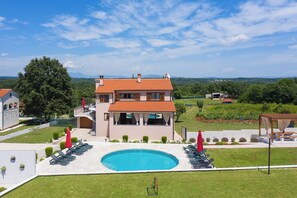 Una casa a due piani con piscina, area salotto esterna e vista sulla campagna.