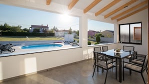 A modern outdoor dining area with a pool, wooden ceiling beams, and a view of the neighborhood.