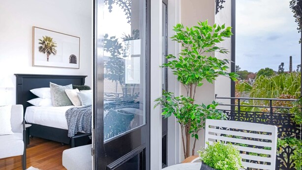 A balcony with a bed, a table, and potted plants. - Designer Styled Studio in Central Trendy Glebe (Glebe)