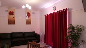 Ein Wohnzimmer mit einer schwarzen Couch, roten Vorhängen, einer Uhr und zwei an der Wand befestigten Blumenbildern.