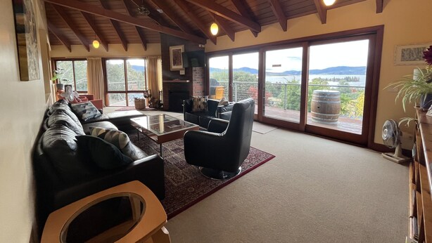 A spacious living room with a fireplace, comfortable seating, and large windows offering a scenic view. - Kurrajong Views Jindabyne (Jindabyne)