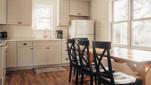 A kitchen with white cabinets, a wooden dining table, and four chairs. - Cozy remodeled modern farmhouse for up to 10, with secondary room for up to 30 (New London)