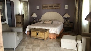 Une chambre à coucher avec un grand lit, deux tables de chevet, une commode en bois et deux fauteuils.