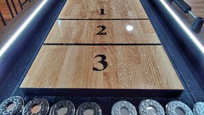 Ett shuffleboard-bord med numrerade områden för poängräkning, en träram och metallbrickor i ändarna.