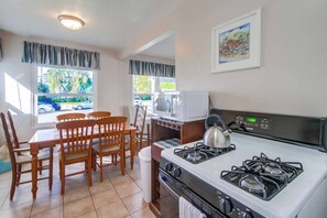 A compact kitchen with a gas stove, microwave, and dining area with wooden chairs. - Charming PB bungalow, pet-friendly yard, parking (San Diego)