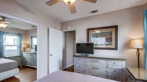 A hotel room with a bed, a television on a dresser, a painting on the wall, and a ceiling fan. - Charming PB bungalow, pet-friendly yard, parking (San Diego)