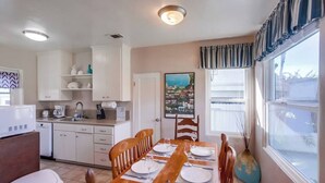 A compact kitchen with white cabinets, a dining table set for four, and a window with curtains. - Charming PB bungalow, pet-friendly yard, parking (San Diego)