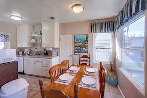 A compact kitchen with white cabinets, a dining table set for four, and a window with curtains. - Charming PB bungalow, pet-friendly yard, parking (San Diego)