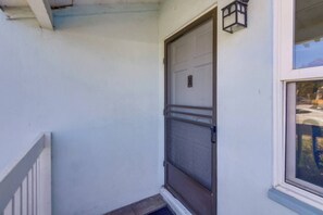 Pared exterior blanca con una puerta cerrada y una ventana que ofrece vistas al exterior.