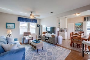 Sala de estar con sofá, televisor, comedor con sillas y zona de cocina con armarios.
