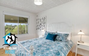 A bedroom with a bed, a nightstand, a lamp, a window, and a wall art piece.