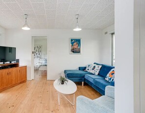 A modern living room with a TV, wooden cabinet, blue sofa, and a small white table.