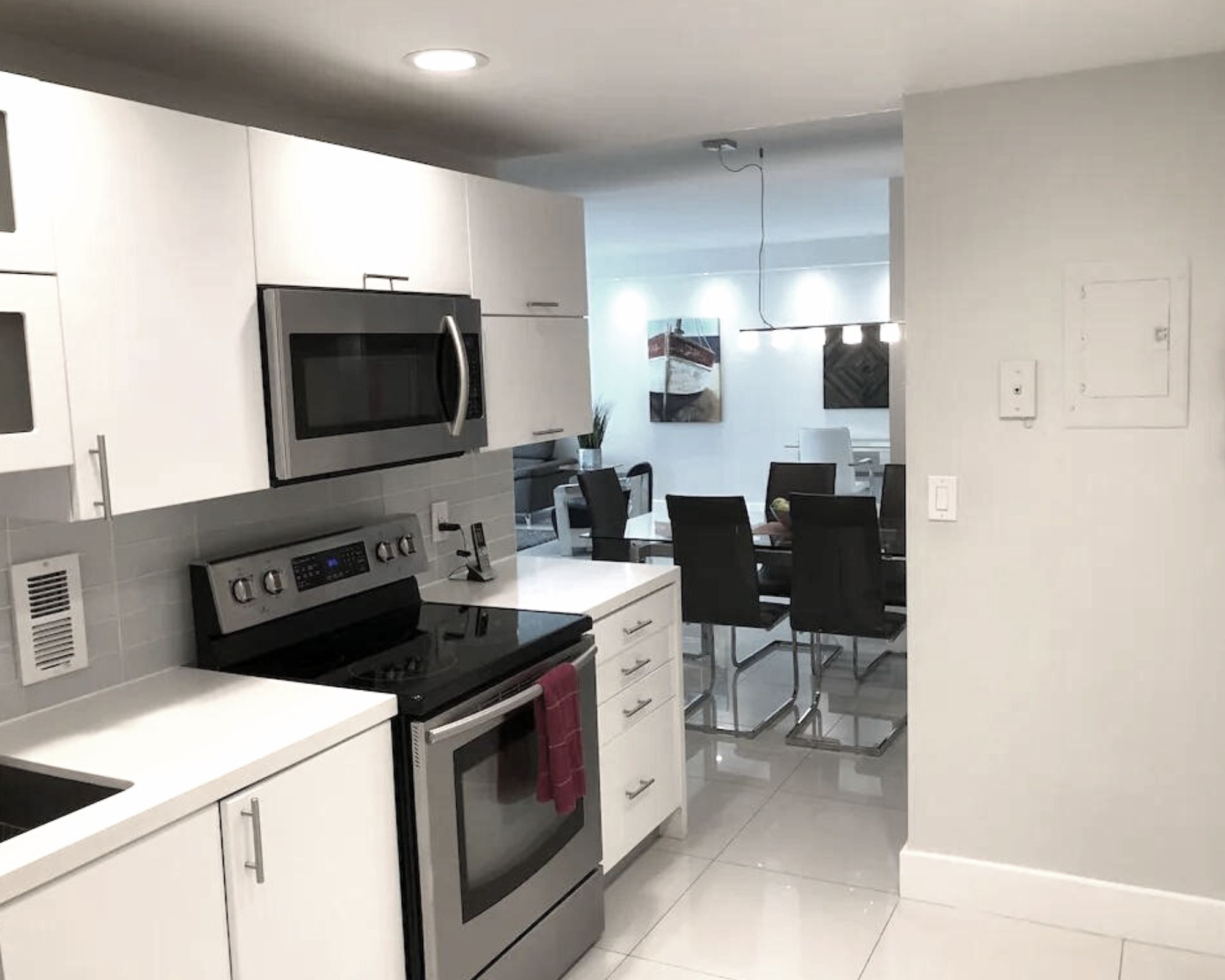 Une cuisine moderne avec des meubles blancs, un four à micro-ondes, une cuisinière et un coin repas comprenant une table et des chaises en verre.