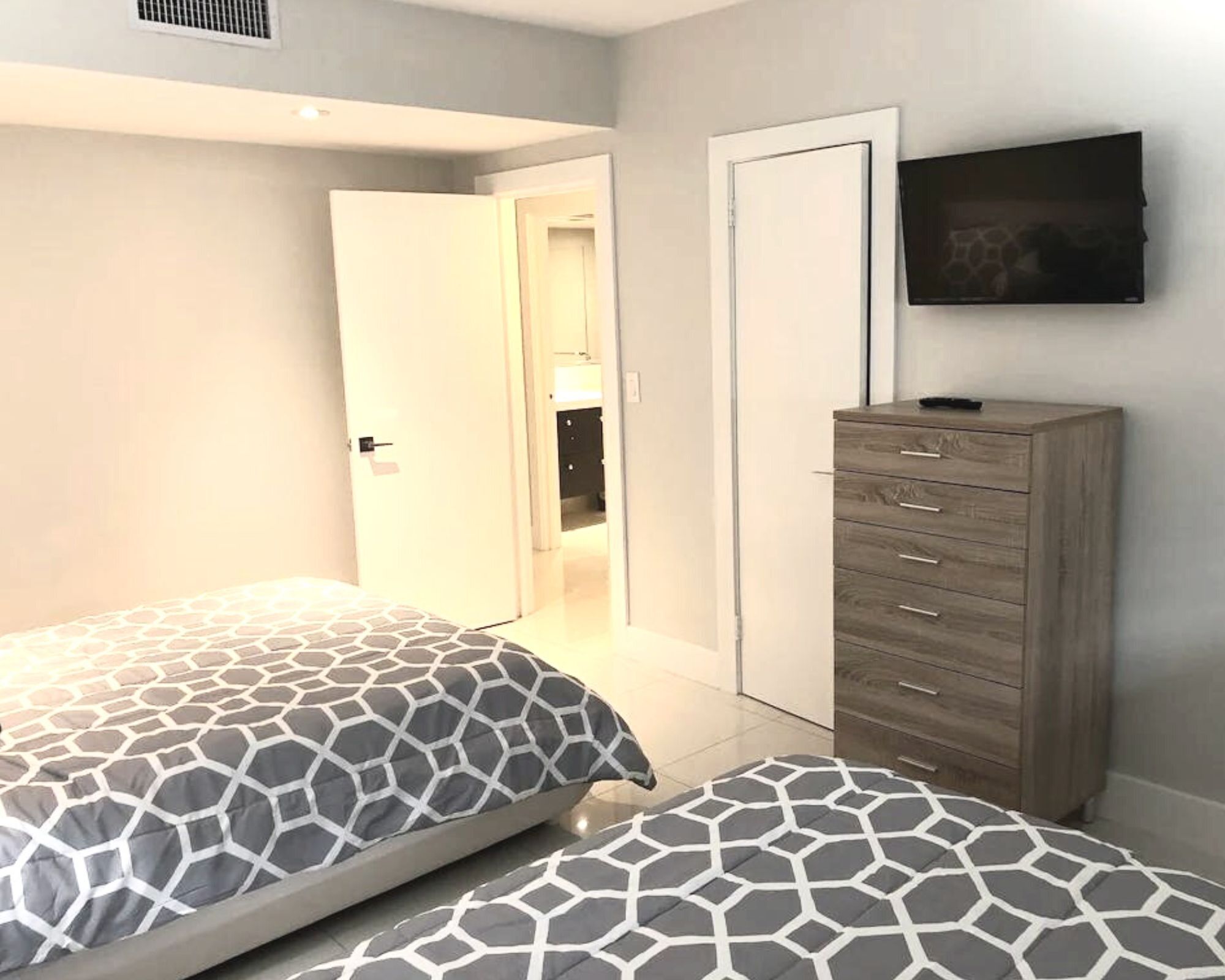 A bedroom with two beds, a dresser, a TV, and a door leading to a bathroom.
