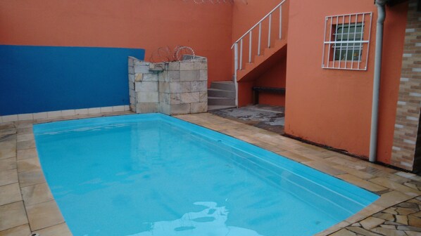 Una piscina con interior azul, rodeada por un deck de piedra y un bajo muro de ladrillo.