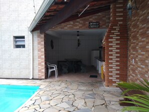 A covered patio area with a stone floor, a pool, and a sign reading "Cantinho do Churro".
