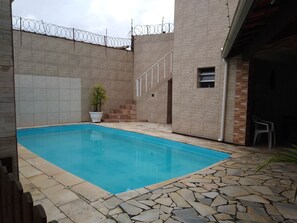 Una piscina con un deck de baldosas de piedra, una escalera y una cerca de alambre de púas.