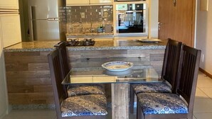 Une cuisine moderne dotée d’un îlot central, de deux suspensions lumineuses et d’un coin repas avec une table à plateau en verre et des chaises à motifs.