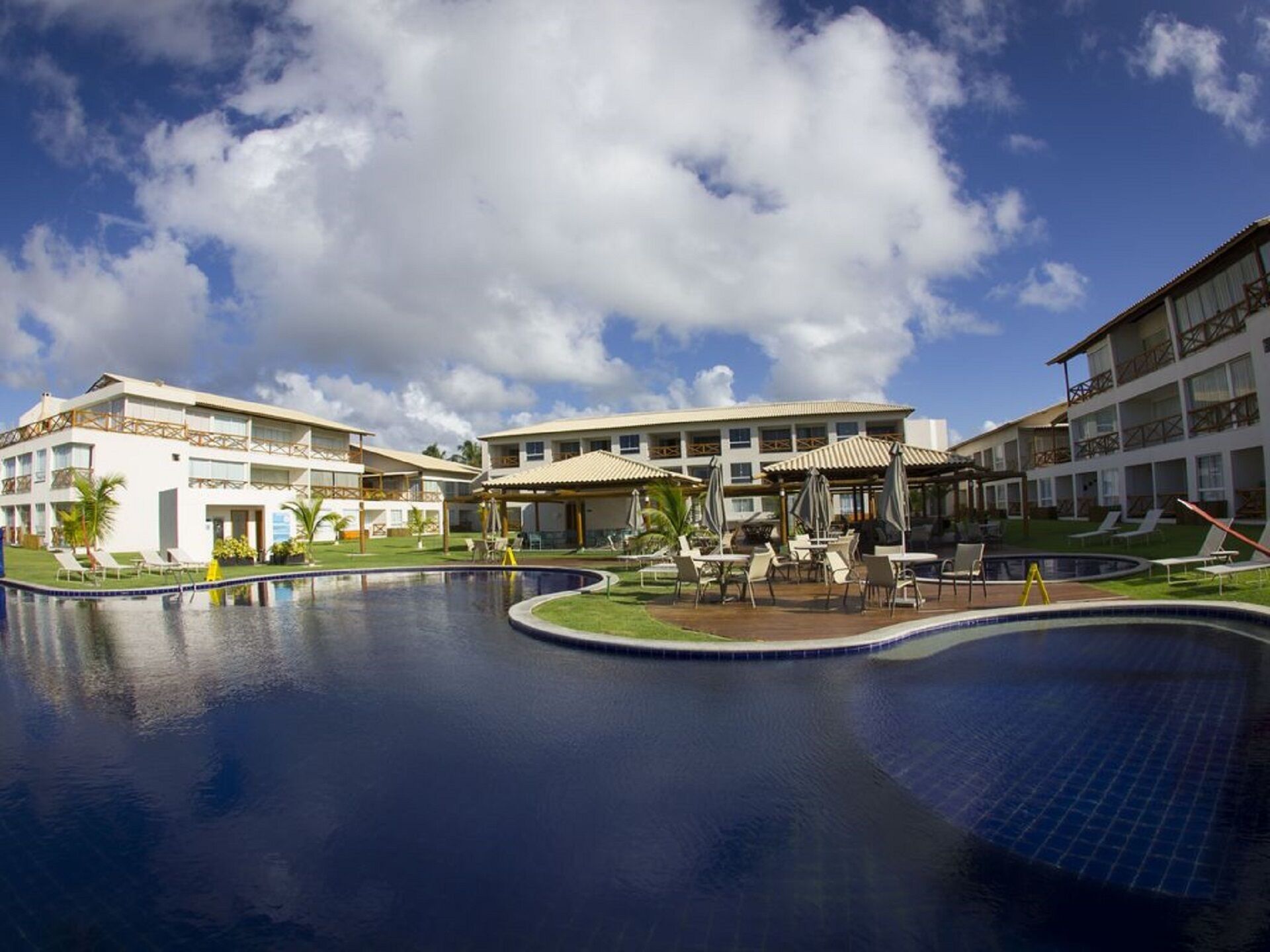 A resort with a large swimming pool, multiple lounge areas, and a building with balconies.