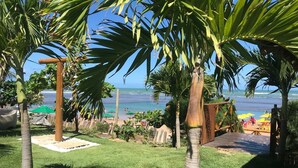 Un jardin tropical agrémenté de palmiers, une terrasse en bois et une vue sur la plage.