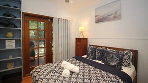 Un dormitorio con cama, mesita de noche, lámpara, estante con adornos y puerta que da a un balcón.