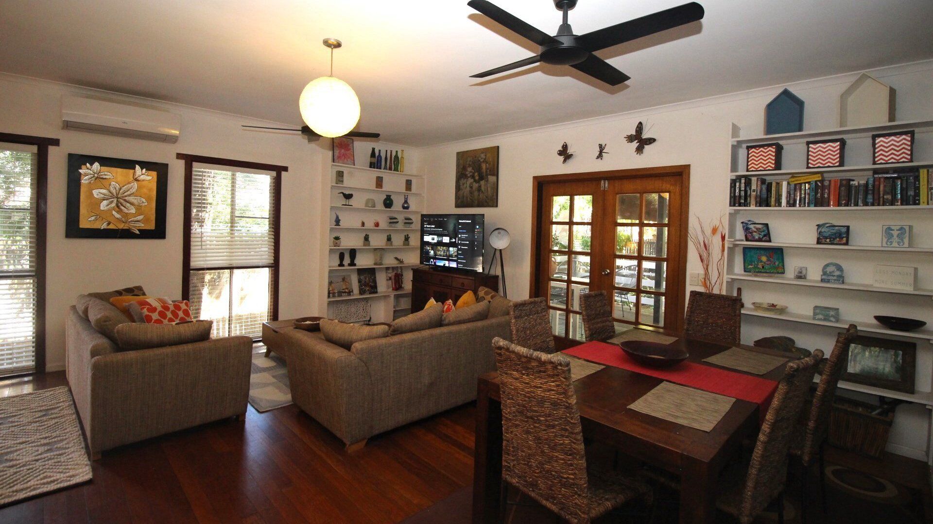 A living room with a sofa set, a dining table with chairs, a ceiling fan, and a bookshelf.