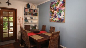 Un comedor con una mesa de madera, sillas de mimbre, una estantería y un colorido cuadro abstracto en la pared.