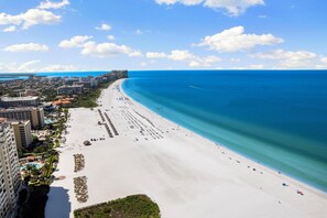 A coastal cityscape with a wide sandy beach, beachfront hotels, and a clear blue sky. - 5 Minute Walk To Beach & JW Marriott, Fantastic SW Pool Exposure, Designer Home (Marco Island)