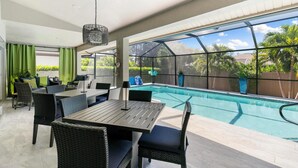 Ett utomhusområde med en pool, ett bord och stolar, omgivet av stora fönster och med utsikt över grönområden.