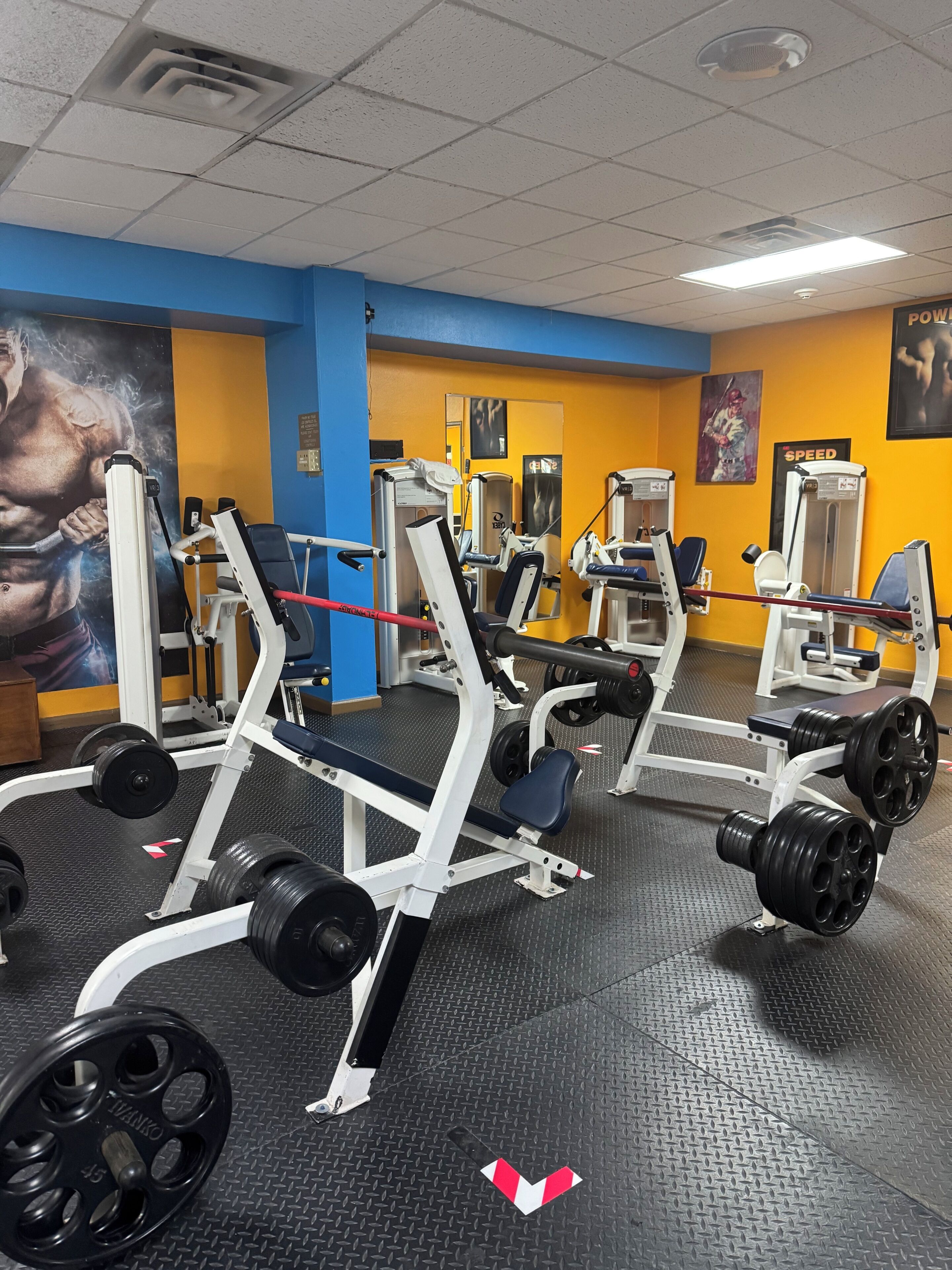 A gym with weightlifting equipment, a mirrored wall, and motivational posters.