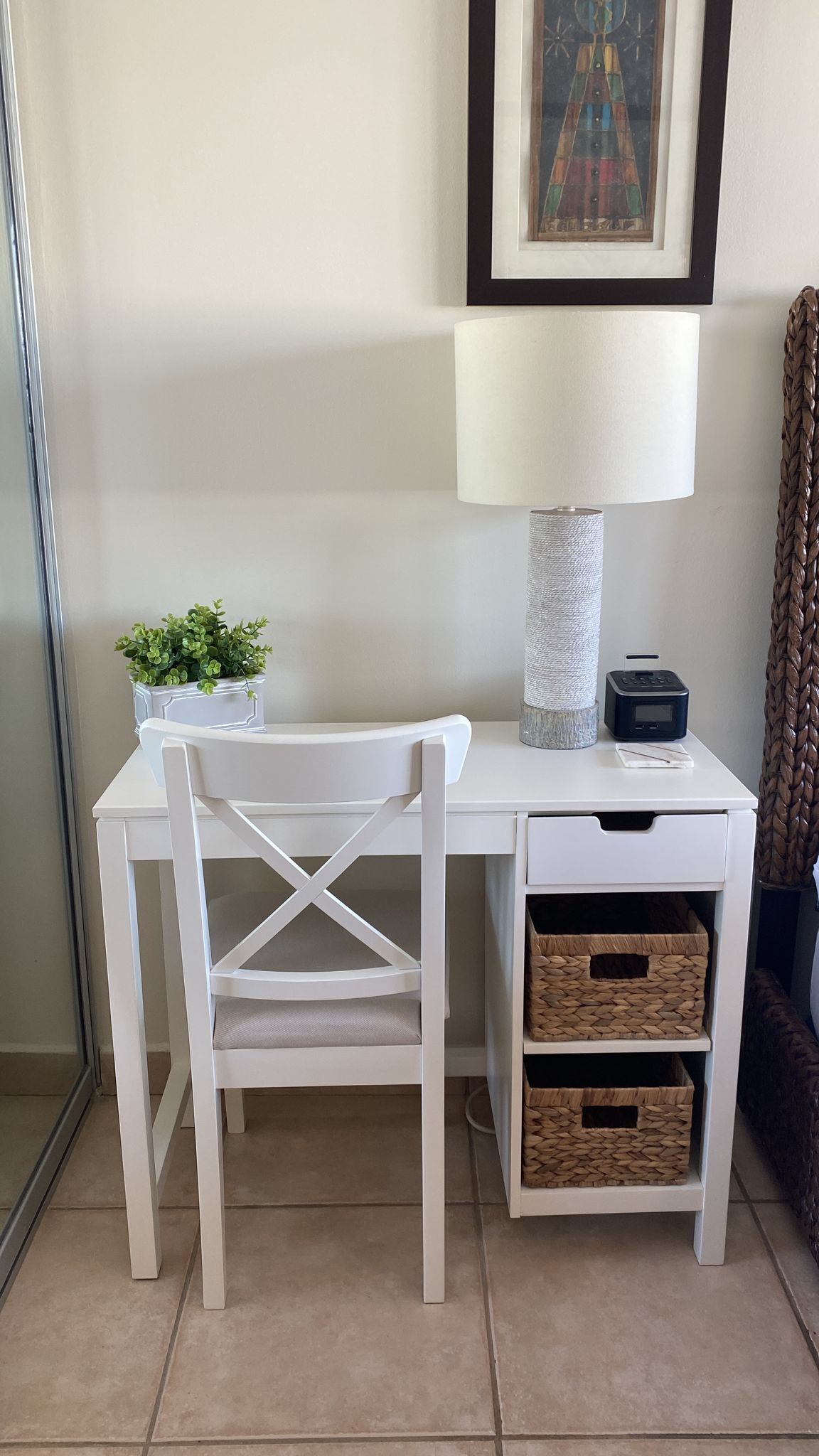 Un bureau blanc avec une lampe, une petite plante et un panier en osier.