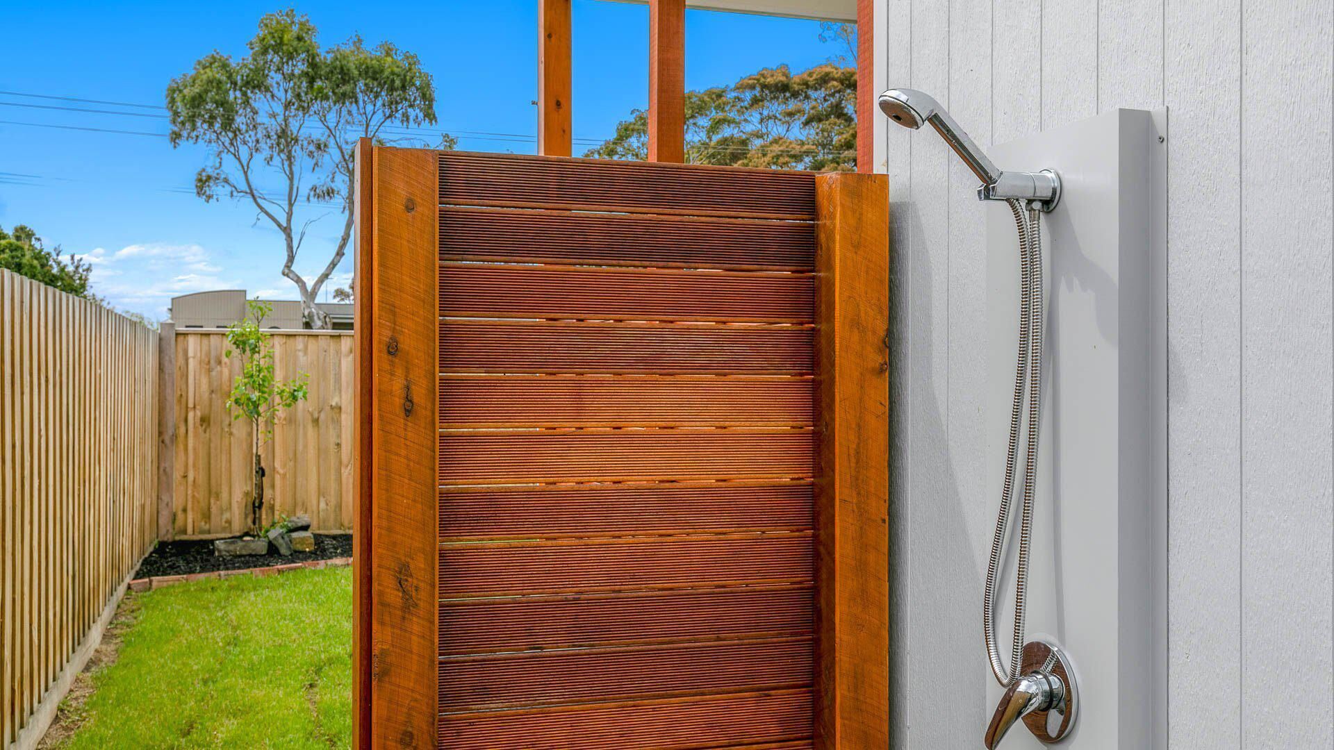 A wooden gate with horizontal slats, a metal showerhead, and a white wall.