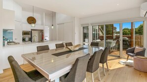 A modern kitchen with a central island, a dining area with a glass table, and a patio with outdoor seating. - Absolutely Beach - with private swimming pool (Cowes)