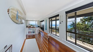 Um corredor espaçoso com piso de madeira, amplas janelas com vista para o oceano e uma área de cozinha moderna, também com vista.
