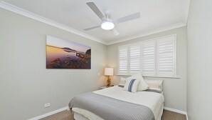 Quarto com cama, ventilador de teto, mesa de cabeceira, luminária e janela com persianas.
