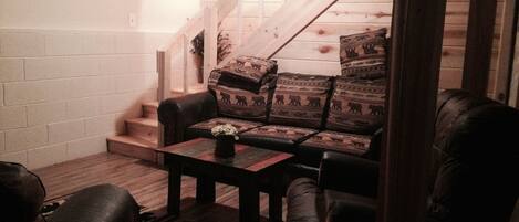 Ein gemütliches Wohnzimmer mit einer Holztreppe, einem Sofa mit gemusterten Kissen und einem Couchtisch mit einer Vase.