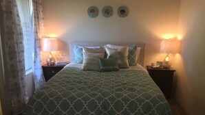 Un lit bien fait, recouvert d’une couvre-lit à motifs, avec deux lampes de chevet et des œuvres d’art décoratives accrochées au mur.