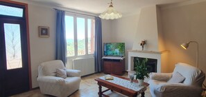 Uma sala de estar com sofá, poltrona, televisão, lareira e vista pela janela.