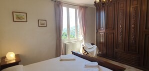 Quarto com uma janela grande, um guarda-roupa de madeira e uma mesa de cabeceira com abajur.