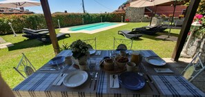 Mesa de jantar montada ao ar livre com vista para uma piscina, cercada por espreguiçadeiras e um muro de pedra.